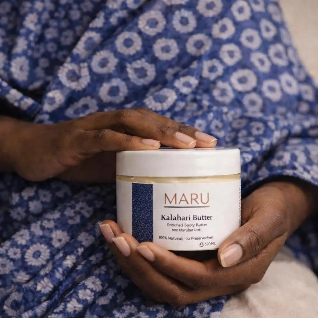 Person holding a container of Maru Kalahari Butter against a blue patterned fabric background
